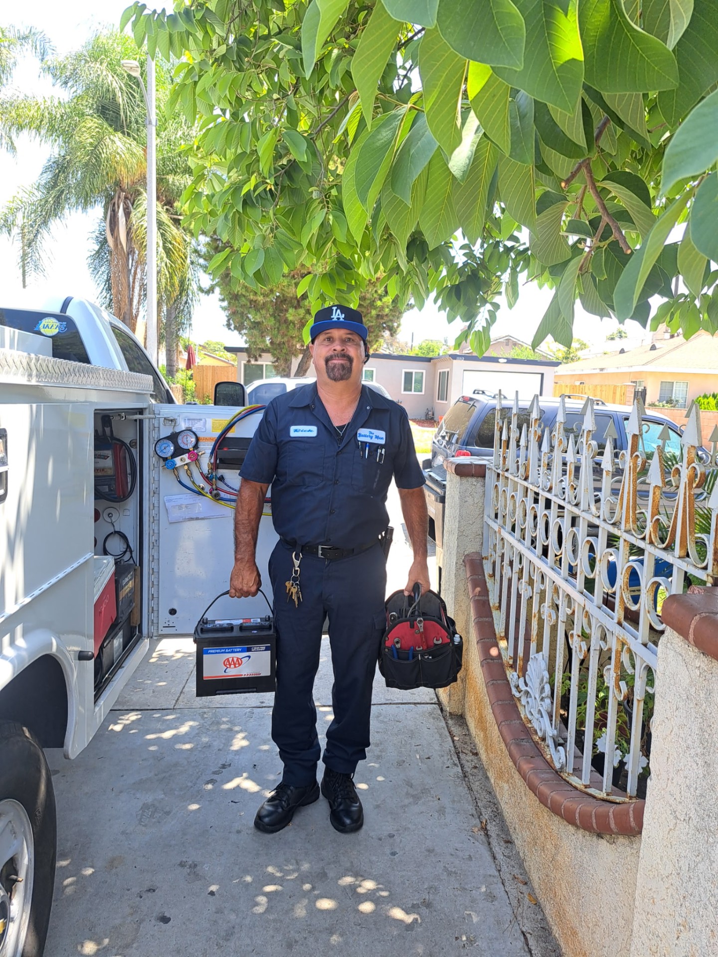 Rick, The Battery Man, holding a car battery and tool bag beside his service truck